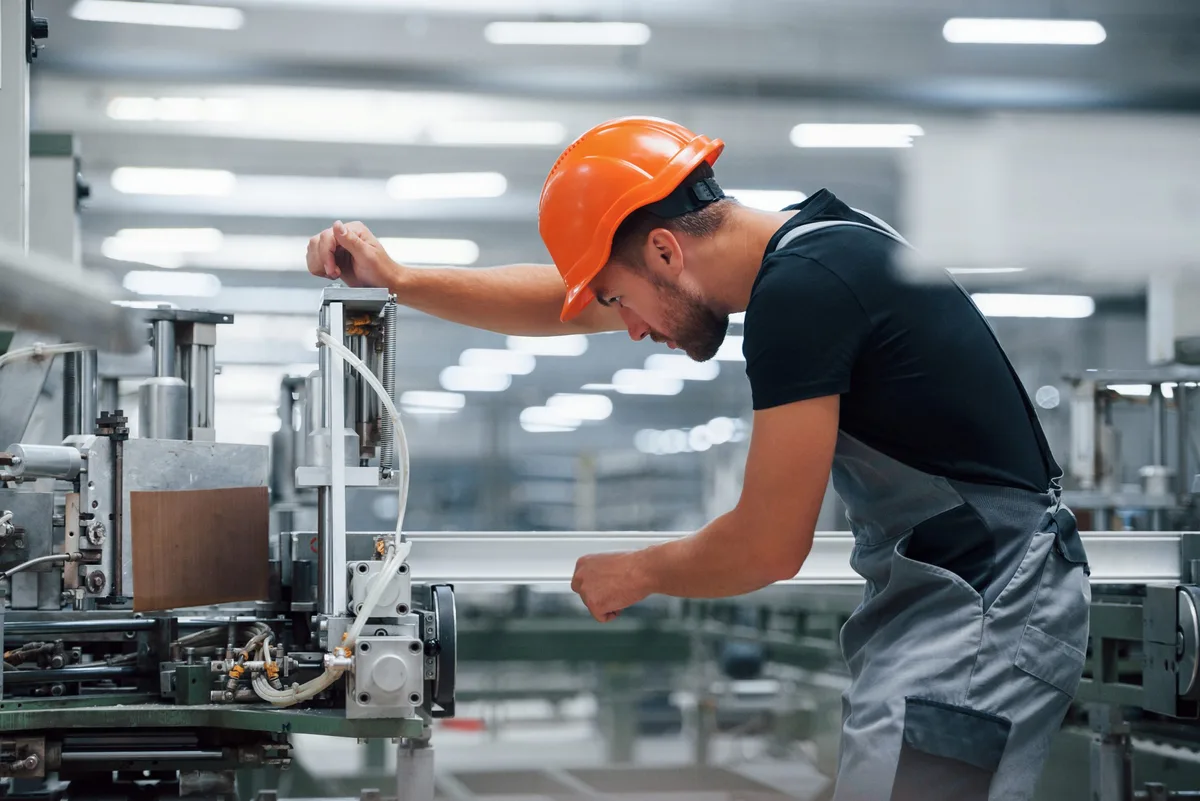 Operator of machine. Industrial worker indoors in factory. Young technician with orange hard hat Die Industrie in Ostwürttemberg blickt positiver in die Zukunft.