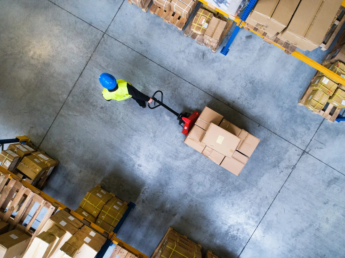 Male warehouse worker pulling a pallet truck. In der Logistik-Branche gibt es aktuell die meisten Arbeitslosen in Ostwürttemberg.