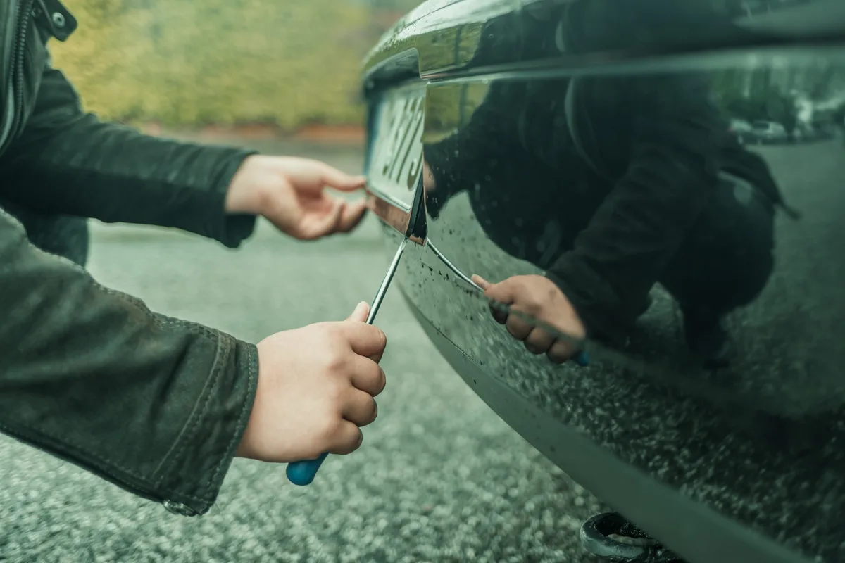 A person steals the license plate on a parked car Unbekannter entwendet Kennzeichen, Symbolfoto.