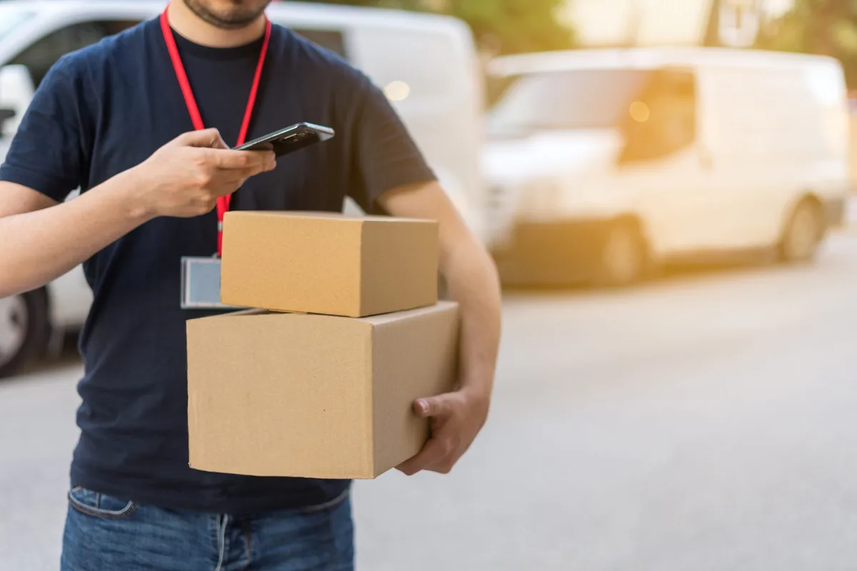 Detalle de mensajero, comprobando la información del pedido para realizar la entrega, en un día soleado. Fotografía horizontal con espacio para texto. Mehr als 50 Lieferungen nahm der junge Betrüger vom Fahrer eines Paketdienstes entgegen.